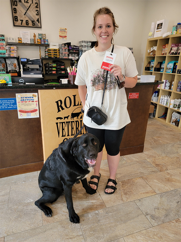 a woman stands beside a black dog in a pet store