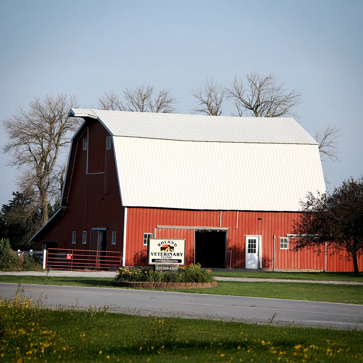 Large red barn with a white roof and the Roland Veterinary Clinic sign in the foreground.