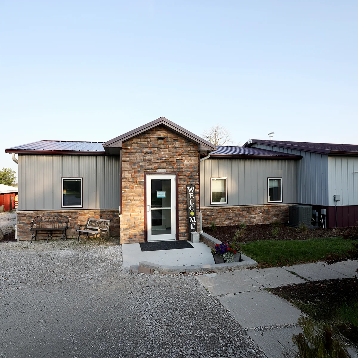 The image shows the entrance to Roland Veterinary Clinic, featuring a modern exterior with stone accents, a “Welcome” sign by the door, and surrounding landscaping.