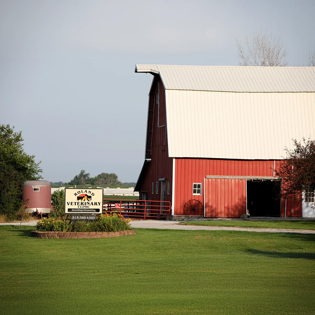 Roland Veterinary Clinic sign in front of a large red barn and green lawn.