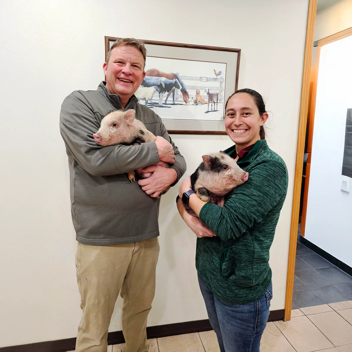 Dr. Robinson and Dr. Goar smiling and holding young piglets indoors.