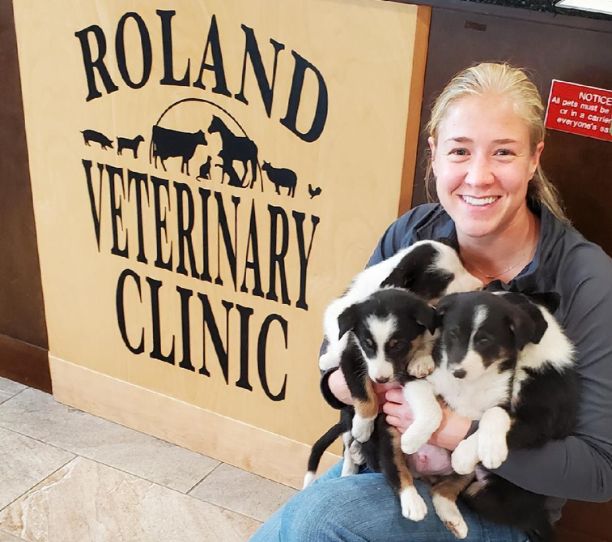 a woman holding two puppies in front of a sign